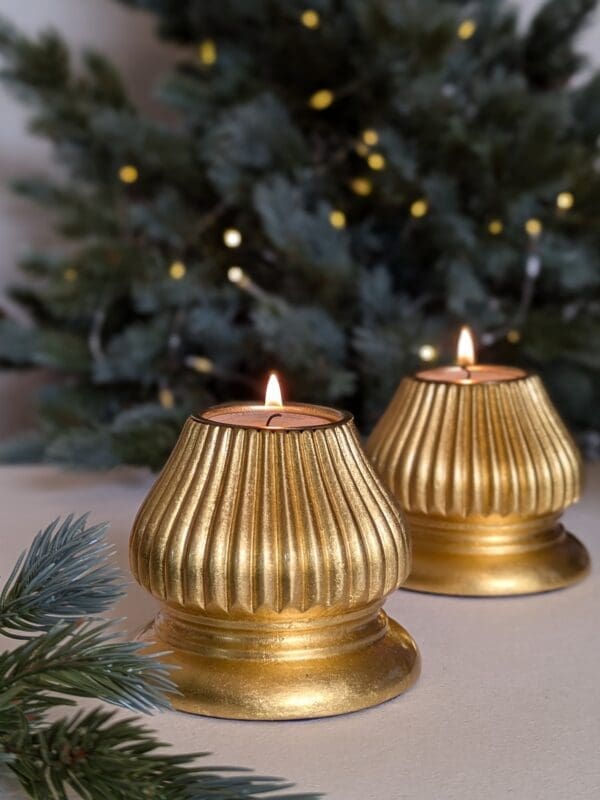 gold fluted candle holders in front of christmas tree with lights