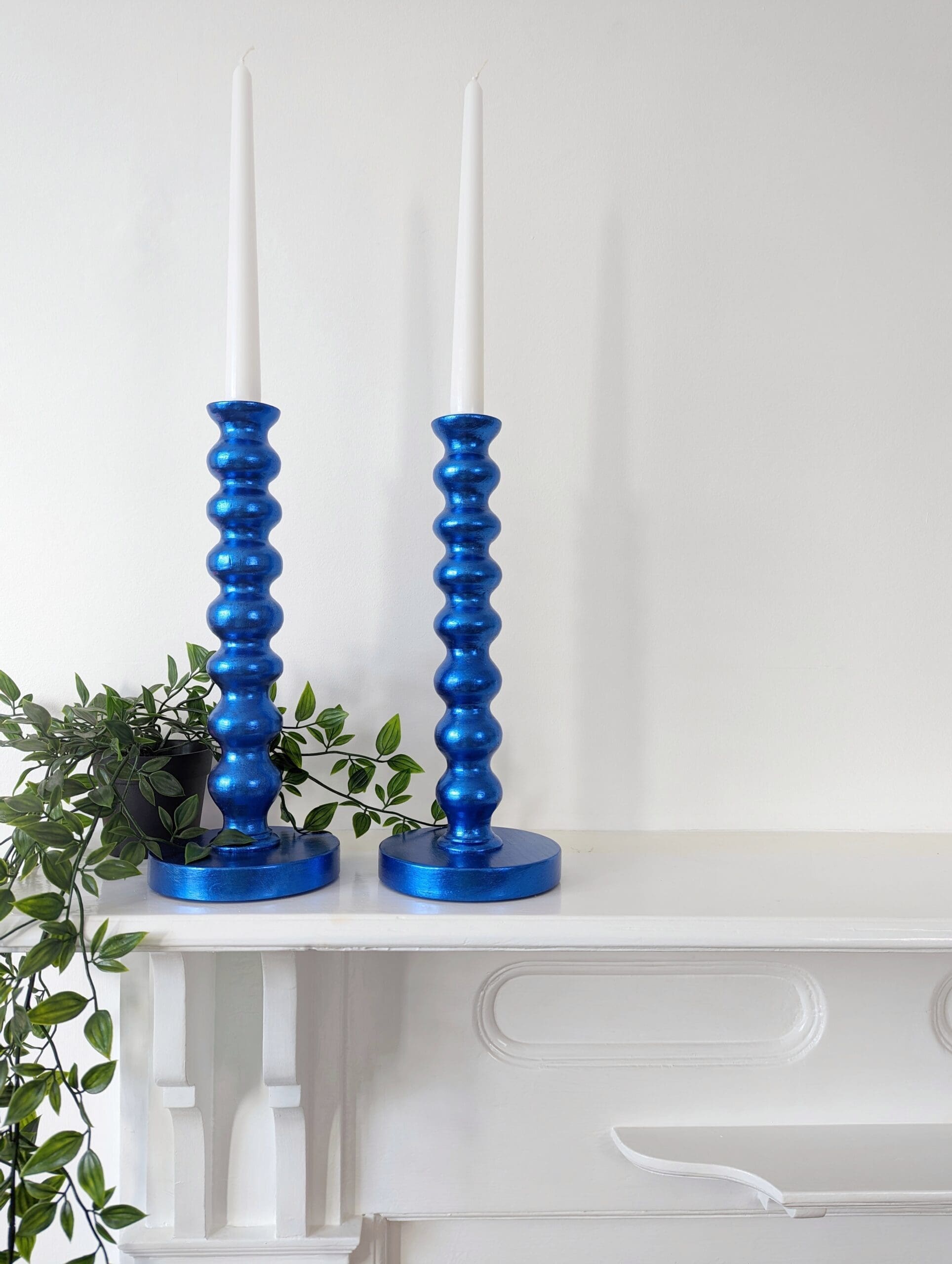 Metallic royal blue bobbin candlesticks on mantlepiece with trailing plant