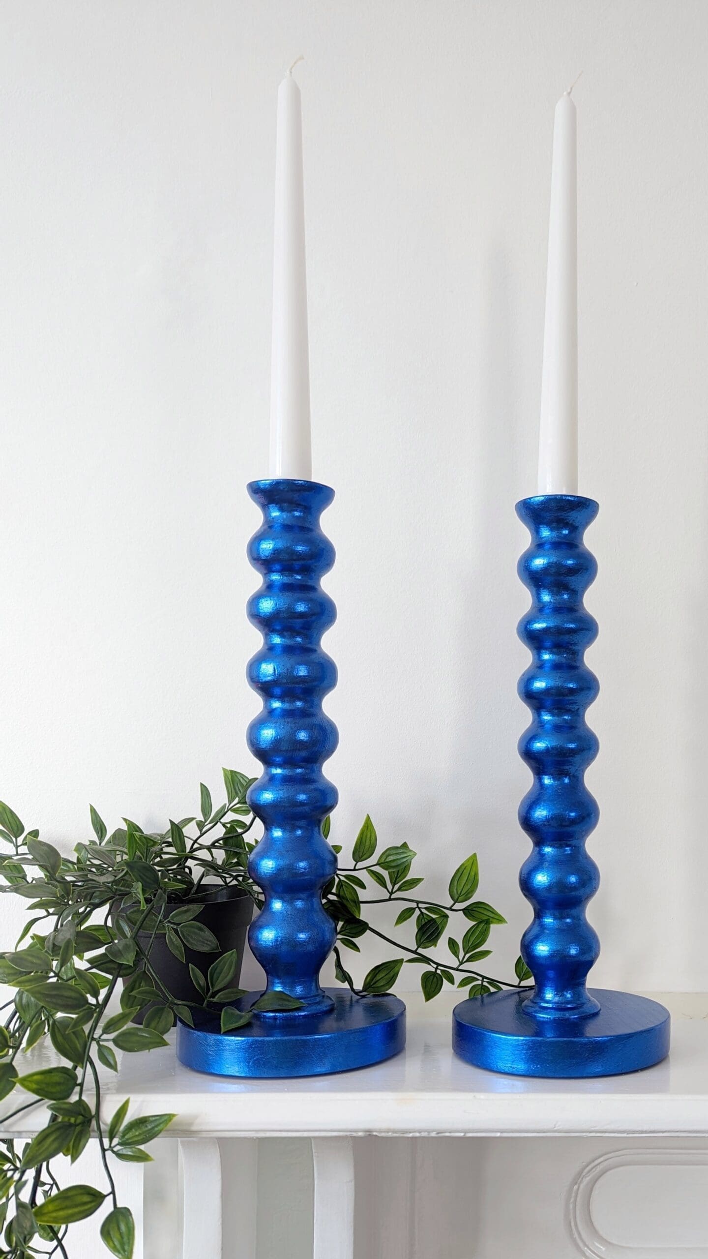 Metallic royal blue bobbin candlesticks on mantlepiece with trailing plant