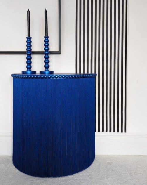 Blue console table with long fringing and black and white striped wallpaper