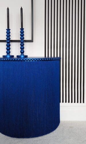 Blue console table with long fringing and black and white striped wallpaper