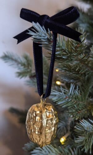 Gold walnut decoration with navy velvet bow hanging on a Christmas tree