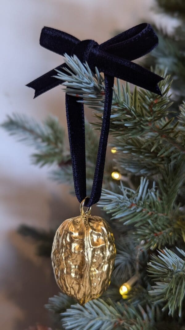 Gold walnut decoration with navy velvet bow hanging on a Christmas tree