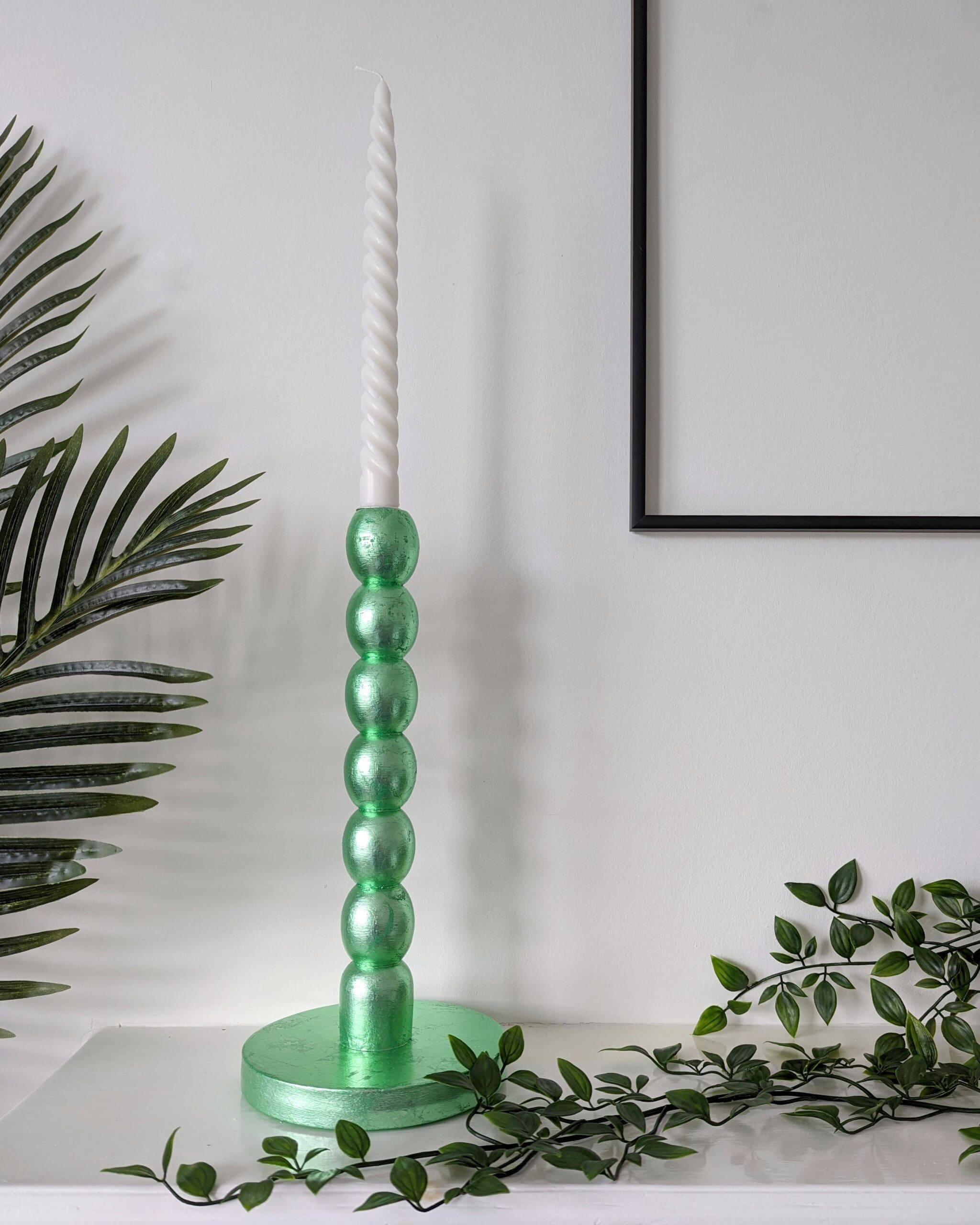 Metallic mint green bobbin candlesticks on mantlepiece with trailing plant