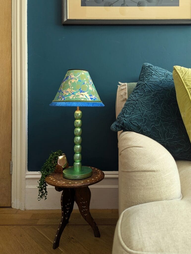 Cordless green bobbin lamp with marbled lampshade sitting on small table next to a sofa