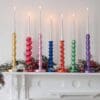 Gilded reclaimed candlesticks in different colours on a mantlepiece with a white background