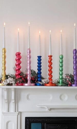 Gilded reclaimed candlesticks in different colours on a mantlepiece with a white background