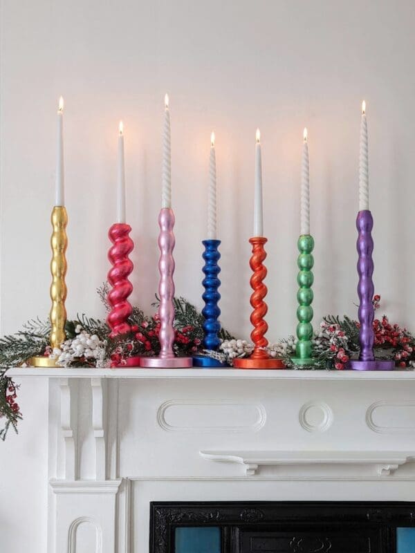 Gilded reclaimed candlesticks in different colours on a mantlepiece with a white background