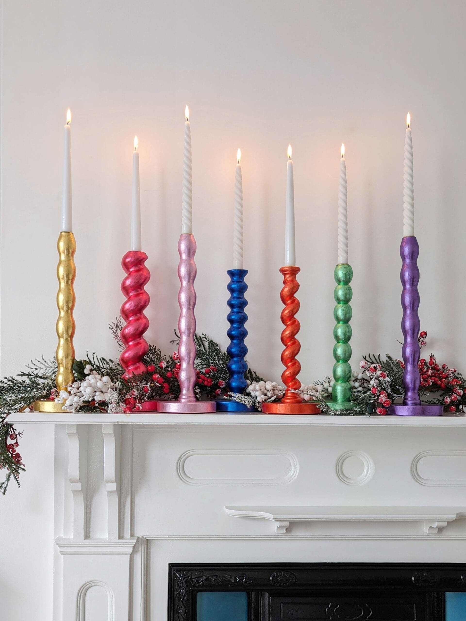 Gilded reclaimed candlesticks in different colours on a mantlepiece with a white background