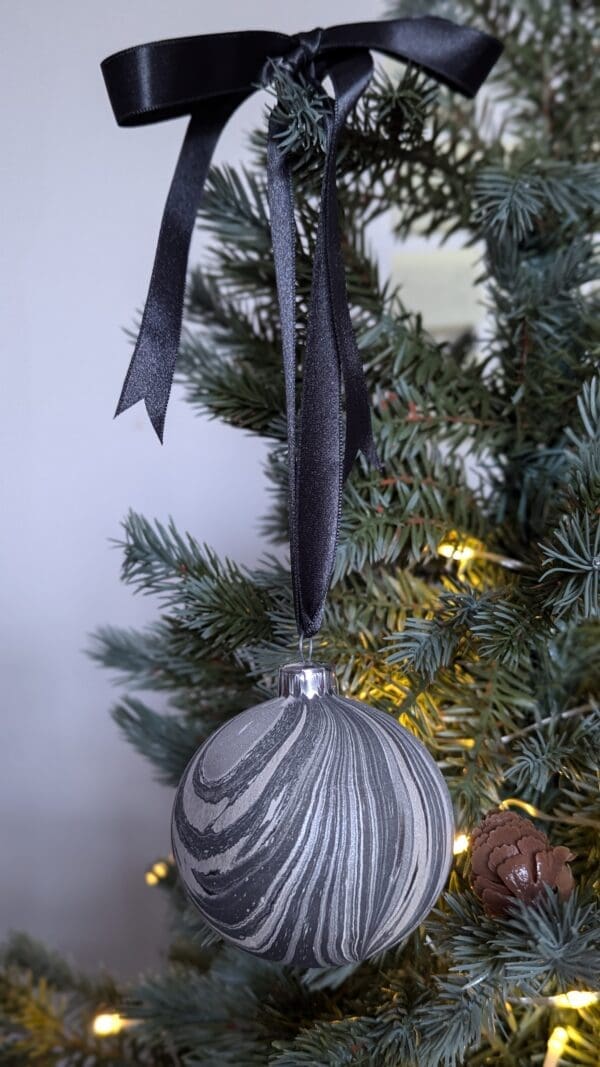 Grey and silver marbled Christmas bauble decoration hanging from dark grey ribbon on a Christmas tree