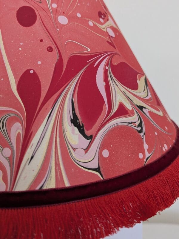 close up of red marbled lampshade showing red fringe trim
