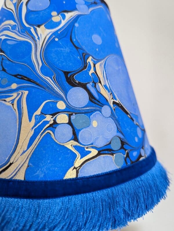 detail of blue and gold marbled paper lampshade with blue fringing and velvet ribbon trim