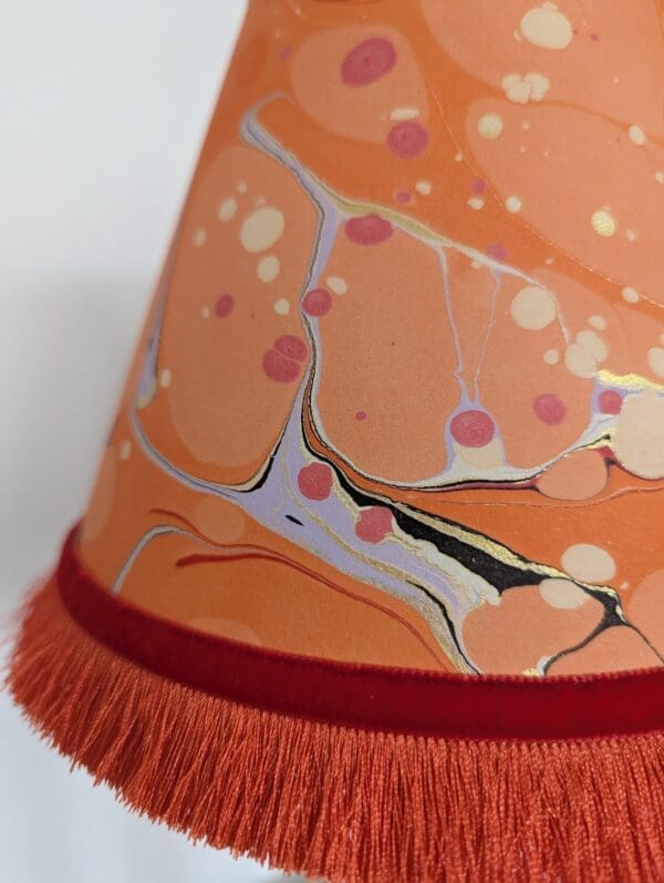 close up of orange marbled paper lampshade showing orange fringing