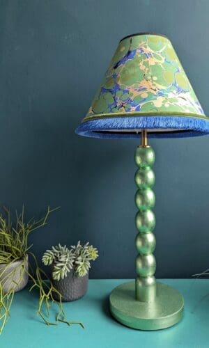 Mint green metallic cordless lamp with green and blue marbled lampshade against dark green wall