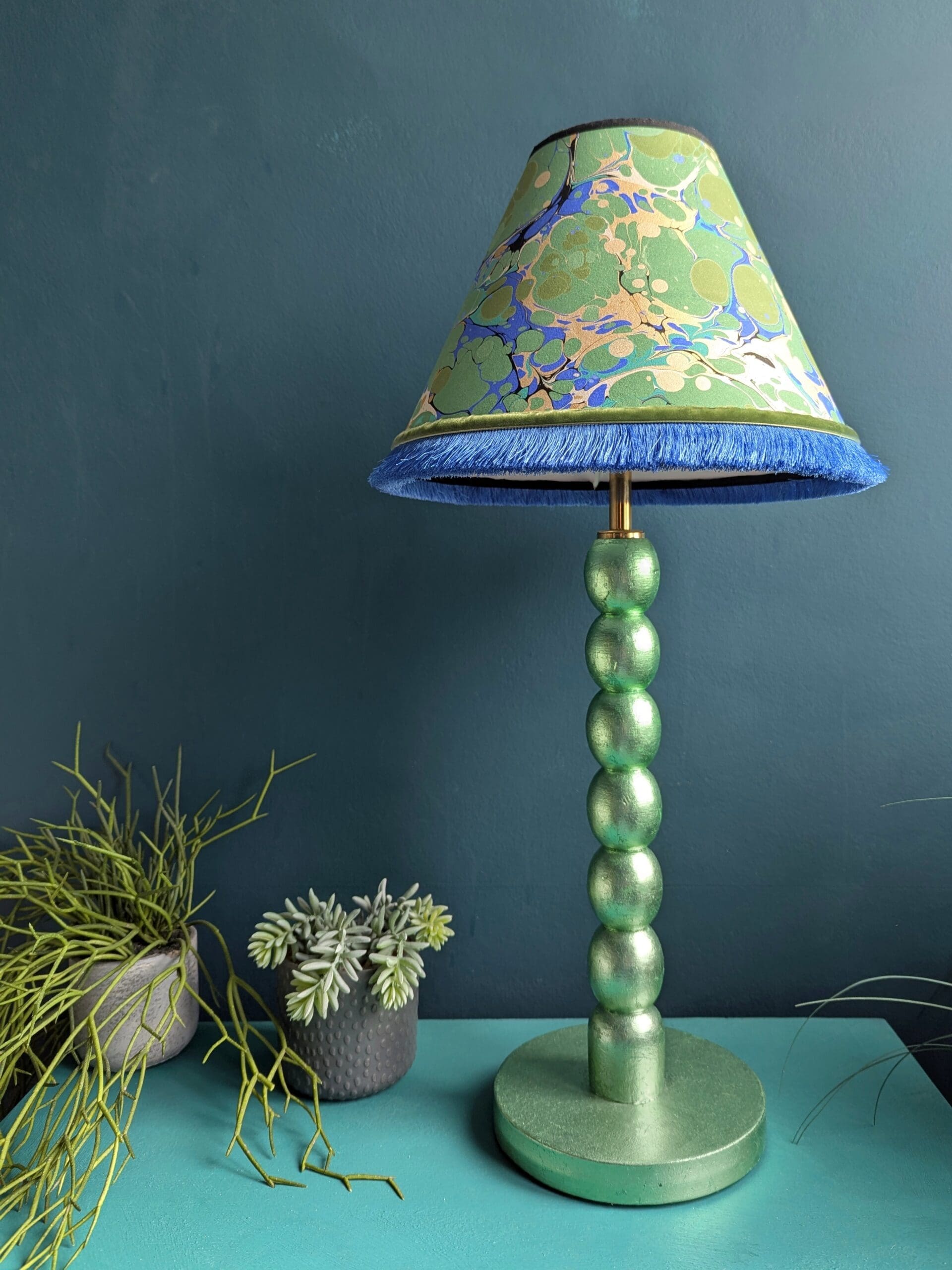 Mint green metallic cordless lamp with green and blue marbled lampshade against dark green wall