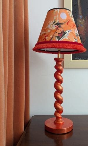 Orange gilded barley twist lamp with marbled paper shade on wooden cabinet with orange velvet curtain