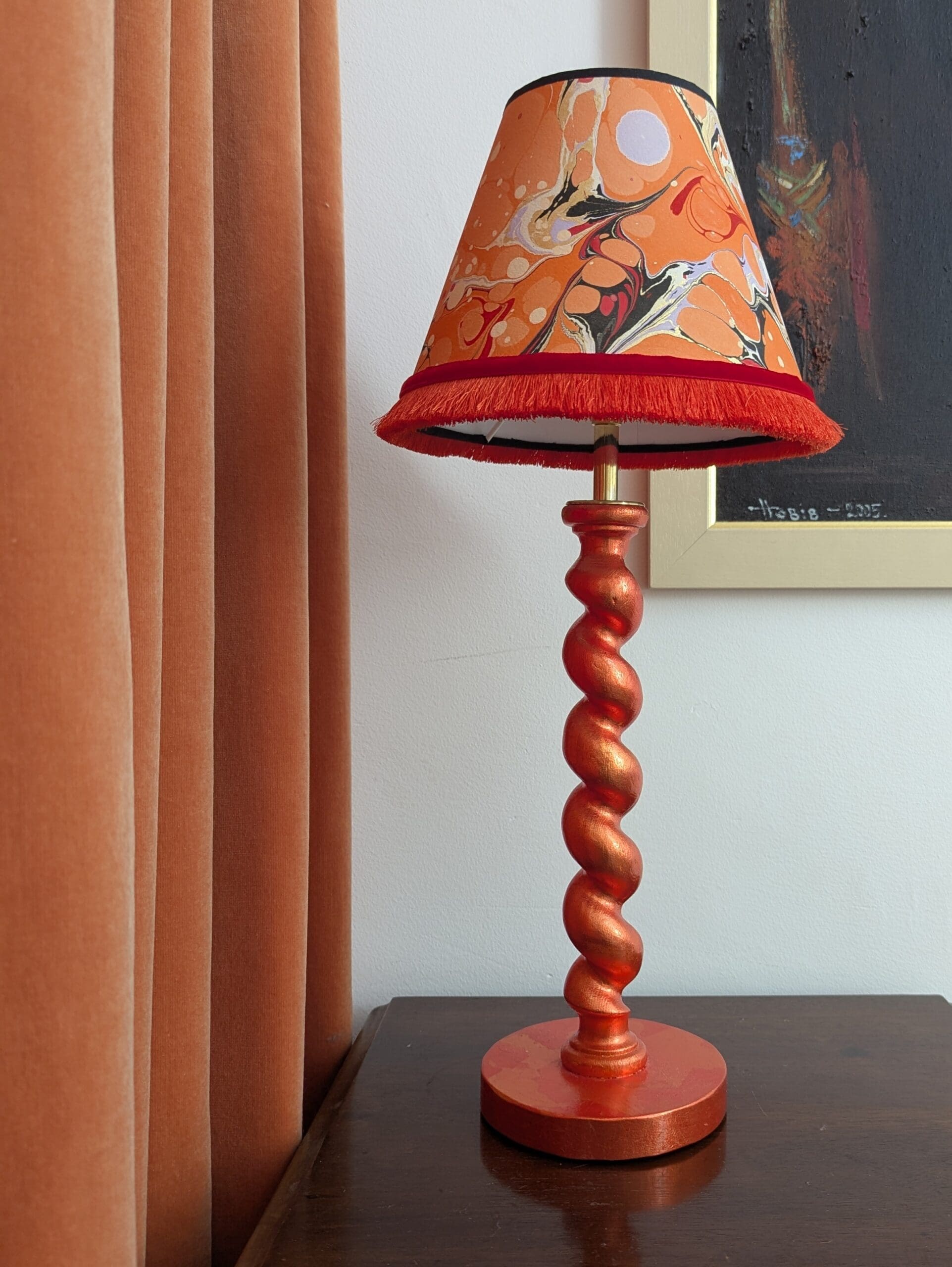 Orange gilded barley twist lamp with marbled paper shade on wooden cabinet with orange velvet curtain