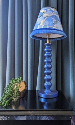 Blue gilded cordless lamp wit blue marbled lampshade on black cabinet in front of blue velvet curtain