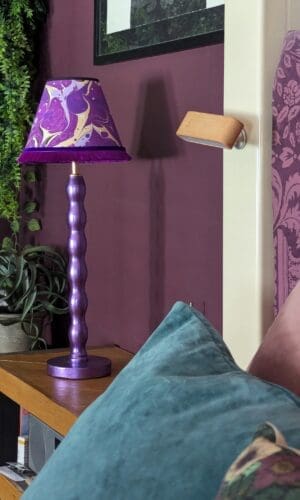 Metallic purple bedside lamp with purple marble lampshade next to a bed with teal cushion