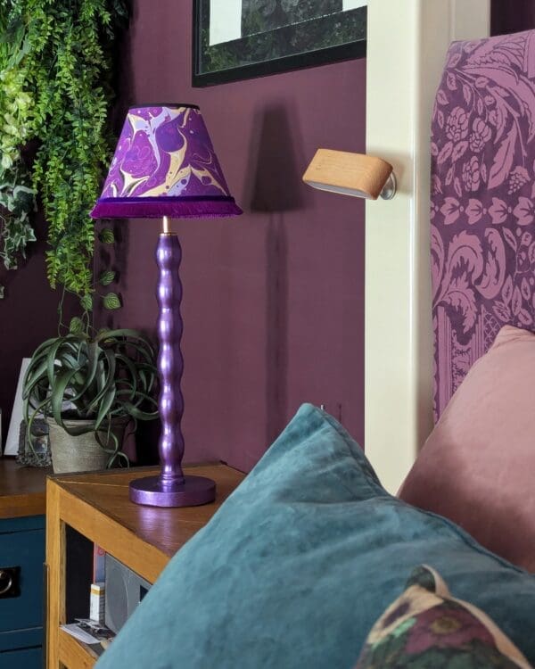 Metallic purple bedside lamp with purple marble lampshade next to a bed with teal cushion