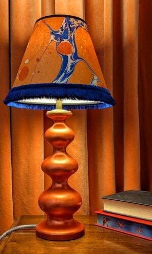 orange curvy lamp with orange and blue marbled shade againt an orange velvet curtin