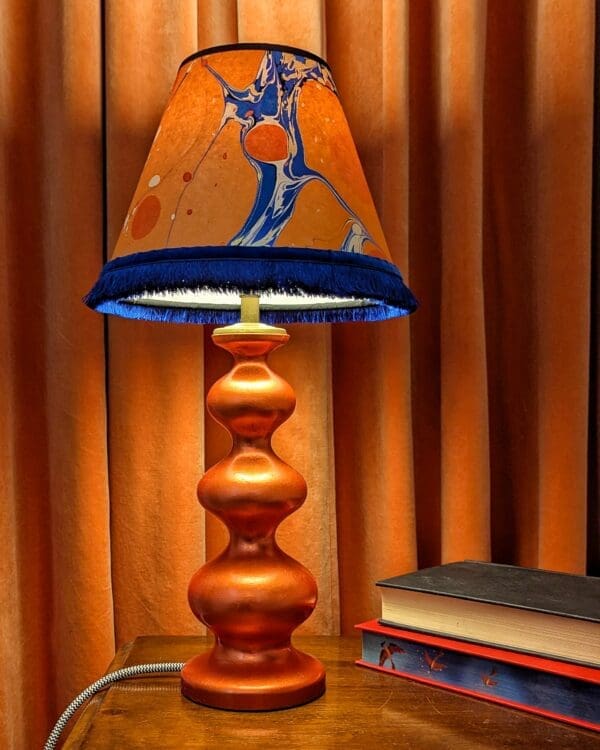 orange curvy lamp with orange and blue marbled shade againt an orange velvet curtin