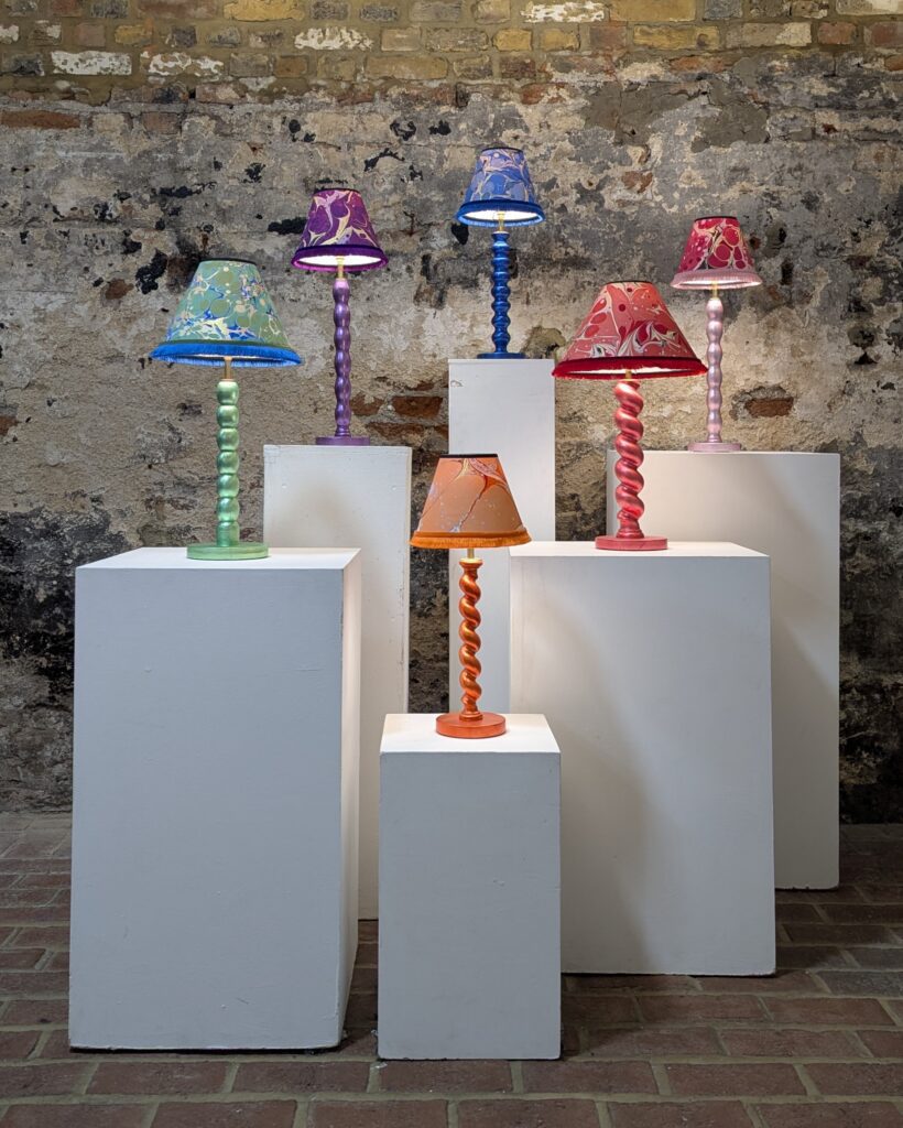 Colourful handmade cordless lamp collection displayed on gallery plinths