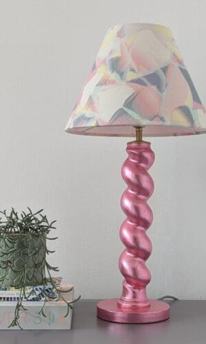 pink twist table lamp with pastel lampshade with books and small plant