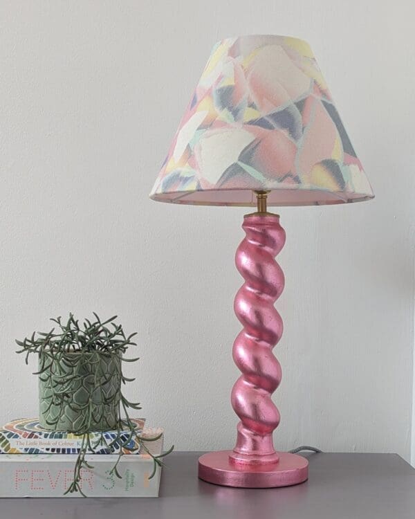 pink twist table lamp with pastel lampshade with books and small plant