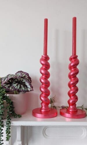 Large metallic red candlesticks on mantlepiece with plants