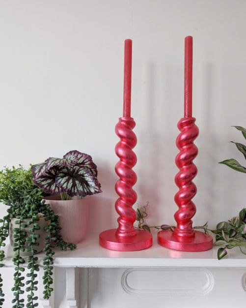 Large metallic red candlesticks on mantlepiece with plants
