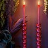 Red metallic barley twist candlesticks with red lit candles agains a maroon background