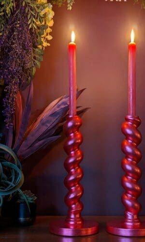 Red metallic barley twist candlesticks with red lit candles agains a maroon background