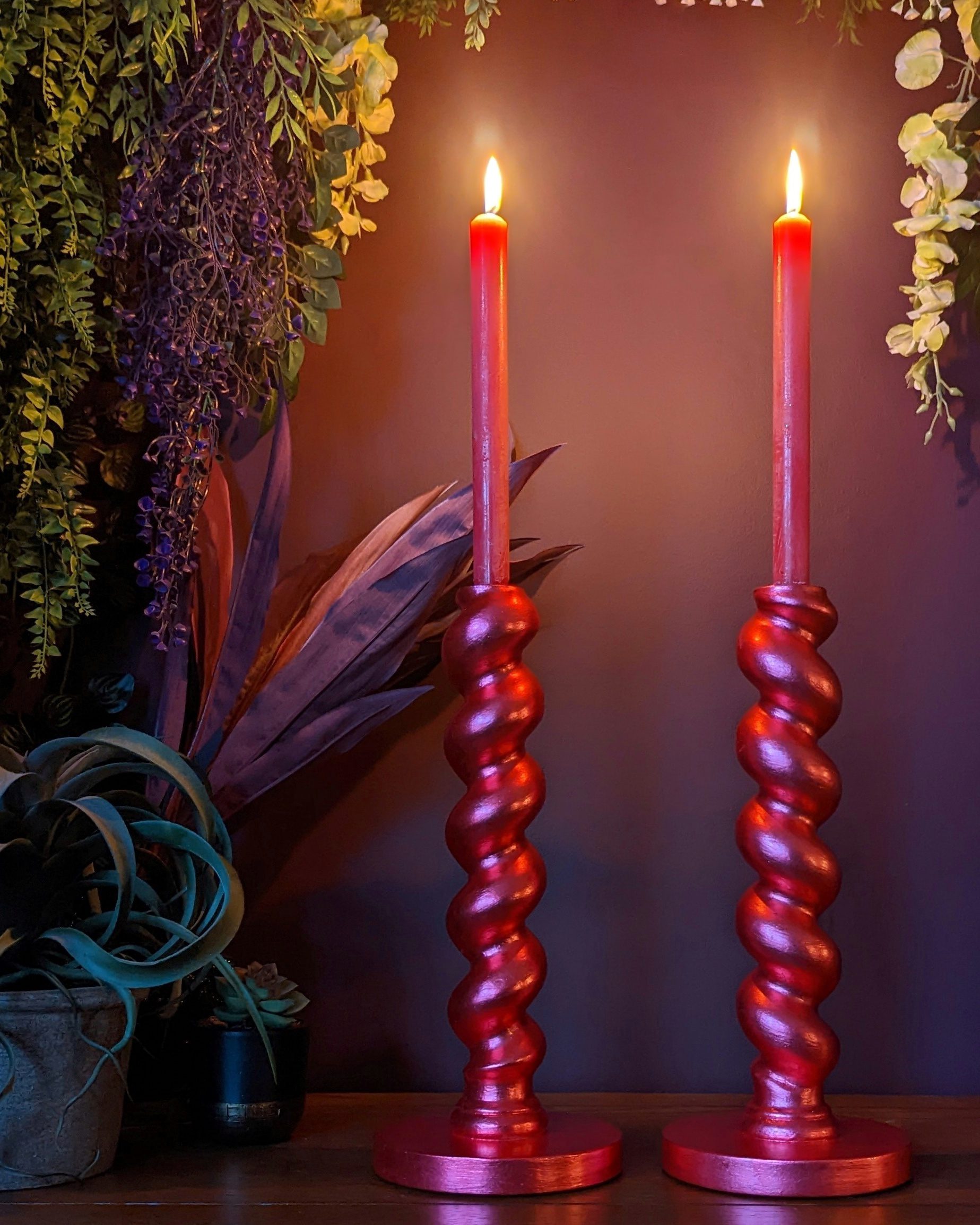 Red metallic barley twist candlesticks with red lit candles agains a maroon background