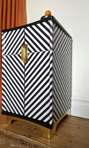 Low angle view of black and white striped drinks cabinet with gold leaf plinth and recessed handles