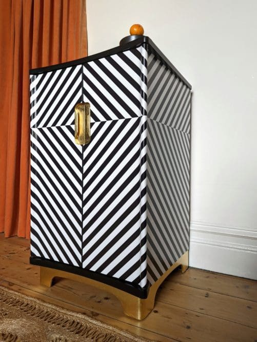 Low angle view of black and white striped drinks cabinet with gold leaf plinth and recessed handles