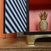 Close up of gold leaf plinth of black and white striped cabinet with door open to show orange interior