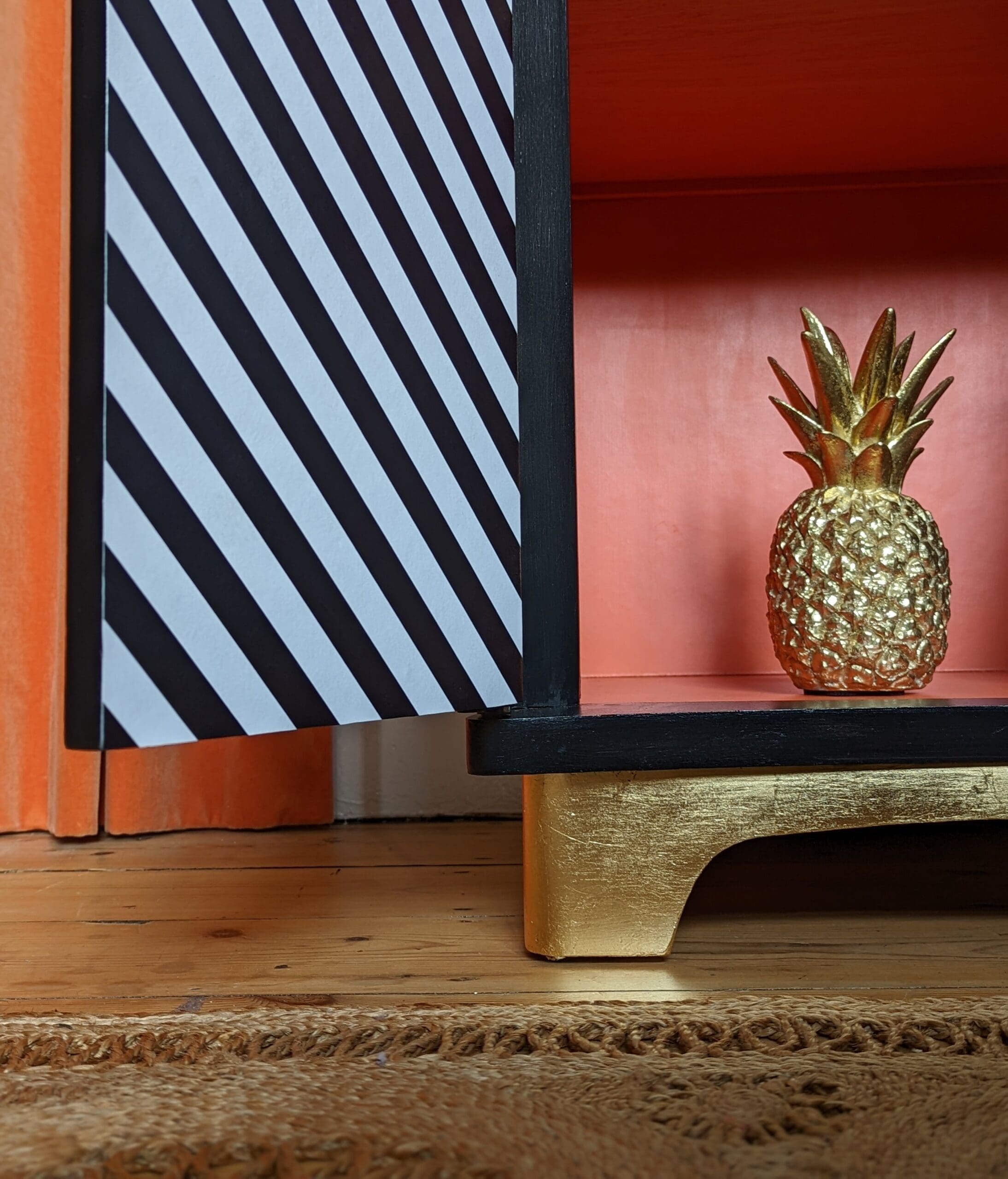 Close up of gold leaf plinth of black and white striped cabinet with door open to show orange interior