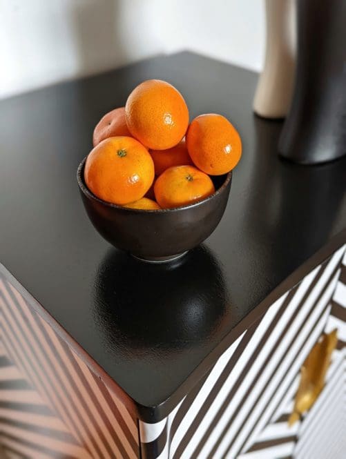 Top view of black and white striped cabinet showing shiney black finish and a bowl or oranges