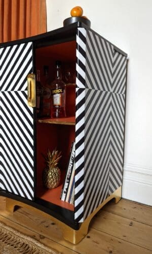 Angle view of monochrome striped drinks cabinet with one door open showing orange interior