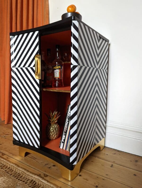 Angle view of monochrome striped drinks cabinet with one door open showing orange interior
