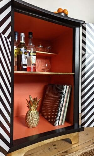 Close up view of inside of geometric striped drinks cabinet showing orange interior and gold details
