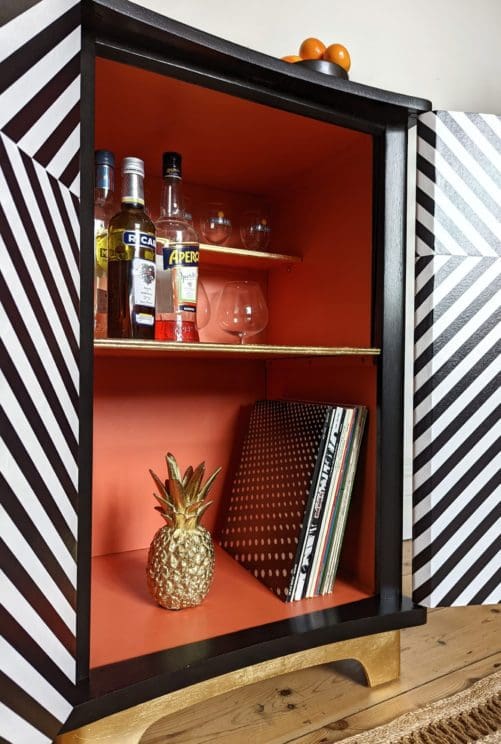 Close up view of inside of geometric striped drinks cabinet showing orange interior and gold details