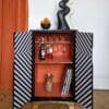 Front view of black and white striped drinks cabinet with doors open to reveal the bright orange interior