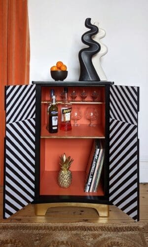 Front view of black and white striped drinks cabinet with doors open to reveal the bright orange interior