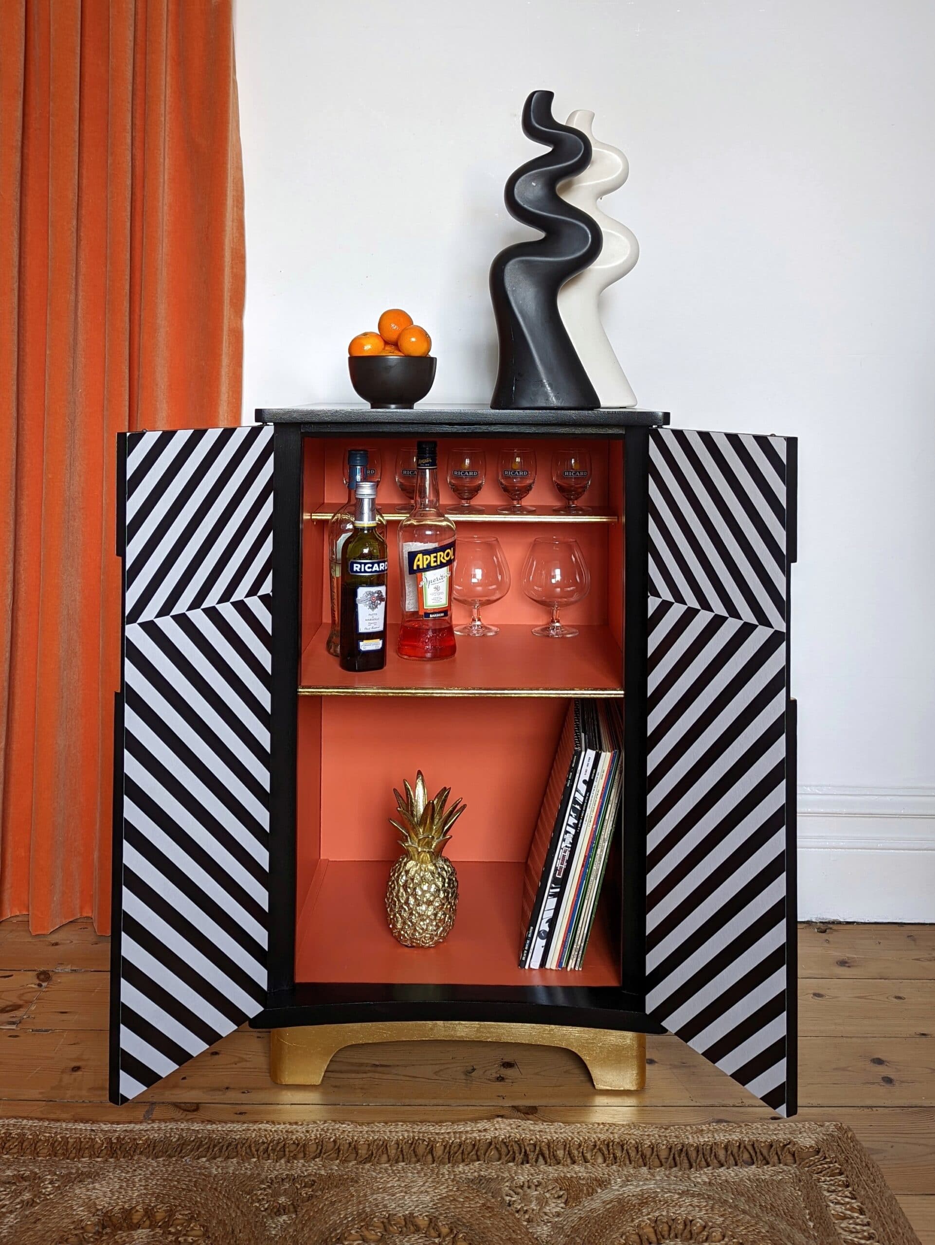 Front view of black and white striped drinks cabinet with doors open to reveal the bright orange interior