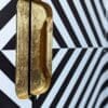 Close up view of recessed gold leaf handles and black and white angled stripe doors to drinks cabinet
