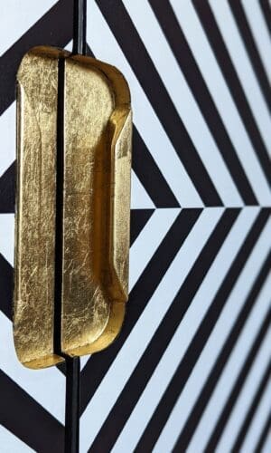 Close up view of recessed gold leaf handles and black and white angled stripe doors to drinks cabinet