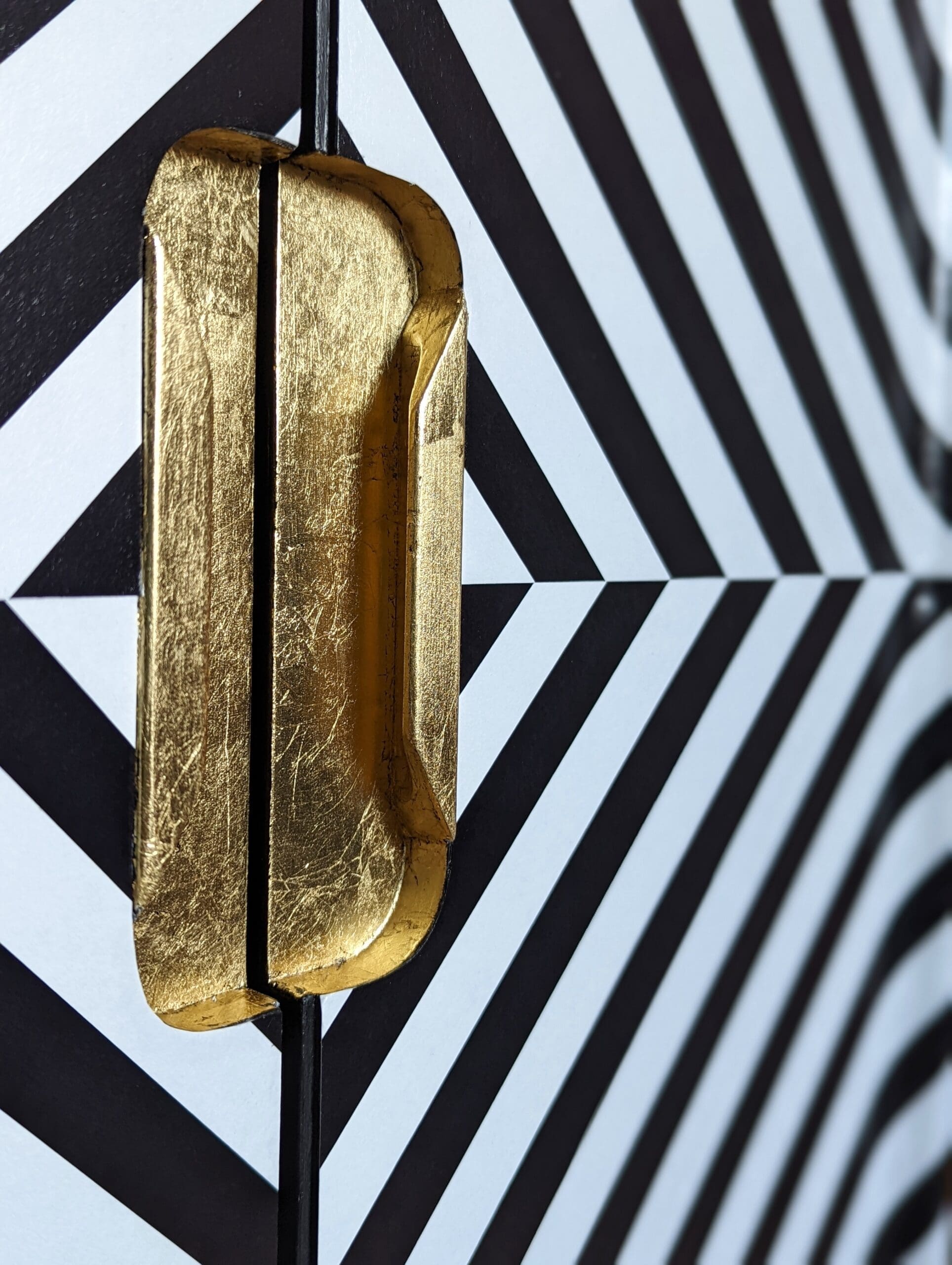 Close up view of recessed gold leaf handles and black and white angled stripe doors to drinks cabinet