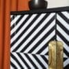 Close up view of gold leaf recessed handles to black and white op-art style cabinet doors